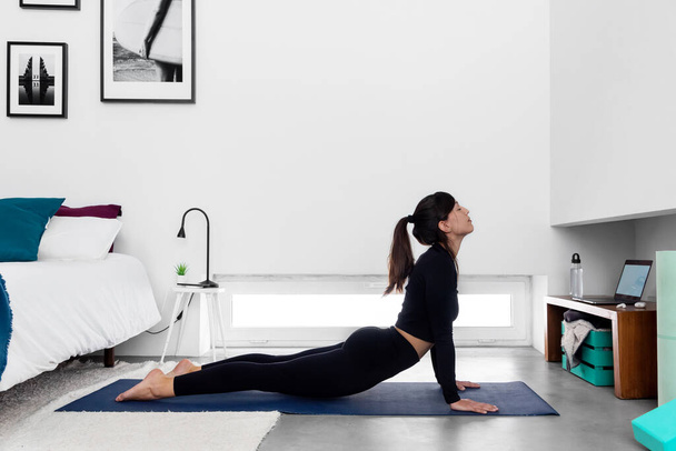 Fit woman practicing Cobra pose using online yoga training program in the laptop at home - Φωτογραφία, εικόνα