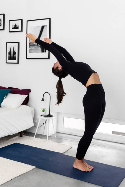 Молодая стройная женщина практикует йогу в современной минималистской спальне дома - Фото, изображение