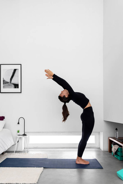 Młoda szczupła kobieta ćwiczy jogę w nowoczesnej minimalistycznej sypialni w domu - Zdjęcie, obraz
