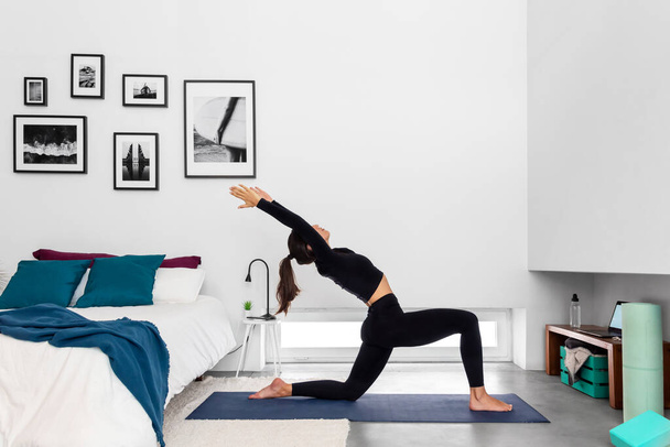 Adatta donna che pratica Half Moon posa utilizzando il programma di formazione di yoga online nel computer portatile a casa - Foto, immagini