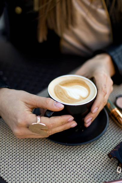 Черная чашка кофе с пеной на сердце в руках молодой девушки вблизи  - Фото, изображение