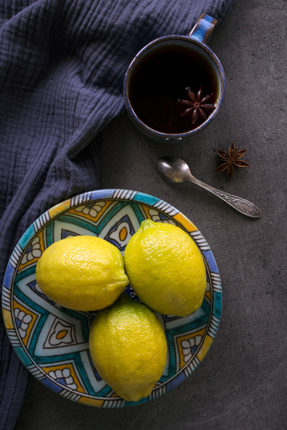 Nature morte avec authentique assiette d'ornement du Moyen-Orient, tasse en céramique bleue, citrons frais et prunes. Fond texturé. Photo colorée.  - Photo, image
