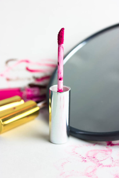 Offenes Rohr mit flüssigem rosa Lipgloss und Lipgloss-Applikator im Fokus. Ein runder Spiegel und Kussabdrücke auf weißem Papier. Dekorative Kosmetik für Frauen. Hochwertiges Foto - Foto, Bild