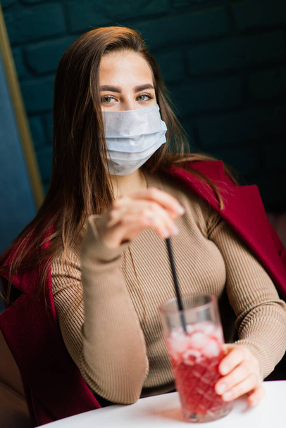 Close up portrait of a caucasian female wearing a medical mask and standing in the street against background of a cafe - Foto, imagen