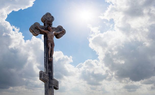 christian cross or crucifix in the rays of the sun against the background of a blue sky with clouds, a symbol of faith in god - Photo, Image