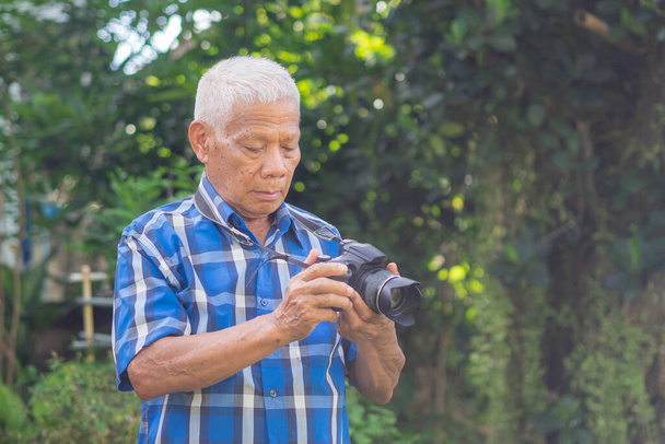 Bahçede dijital kamerayla fotoğraf çeken yaşlı bir adam. Yaşlı bir adam mavi bir gömlek giyer, kamera kullanırken mutludur. Yaşlılar ve fotoğrafçılık kavramı. - Fotoğraf, Görsel