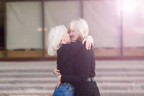 Δύο νεαρά θηλυκά που περπατούν χαμογελώντας αγκαλιάζοντας και φιλώντας εξωτερική - Φωτογραφία, εικόνα
