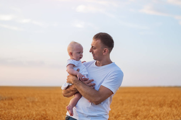Young father tenderly holding baby on wheat field background. Portrait of happy father and child. - Foto, afbeelding