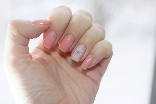 Zimowy manicure na paznokciach na tle zimowego okna. Naturalne odcienie różu i płatków śniegu w kolorze białym z niebieskim kamieniem w postaci lodu na paznokciach. Piękny projekt zimowy manicure. - Zdjęcie, obraz