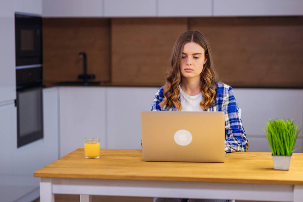 Фокусована молода студентка коледжу, використовуючи ноутбук, друкує під час вивчення роботи .. Серйозна жінка займається інтернет-дослідженнями, сидячи за домашнім офісним столом
. - Фото, зображення