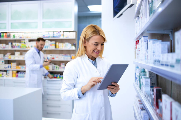 Female pharmacist in white coat checking medicine availability for online orders. Clinical pharmacy concept. - Foto, Imagen