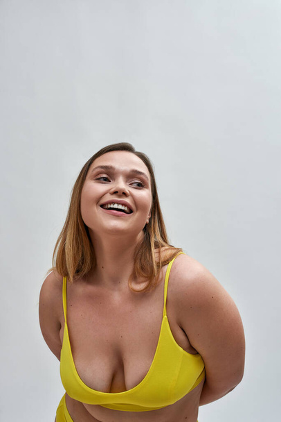 Caucasian young woman wearing yellow bra smiling aside, posing isolated over grey background - Foto, imagen