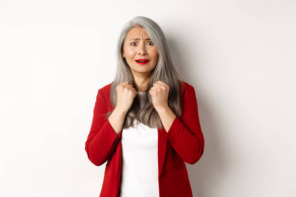 Zakenmensen. Bang volwassen aziatische vrouw kijken doodsbang, beven van angst, staan in rode blazer over witte achtergrond - Foto, afbeelding