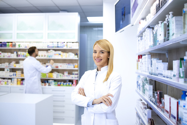 Portrait of professional woman pharmacist proudly standing in pharmacy shop or drugstore. In background shelves with medicines. Healthcare and medicine. - Photo, Image