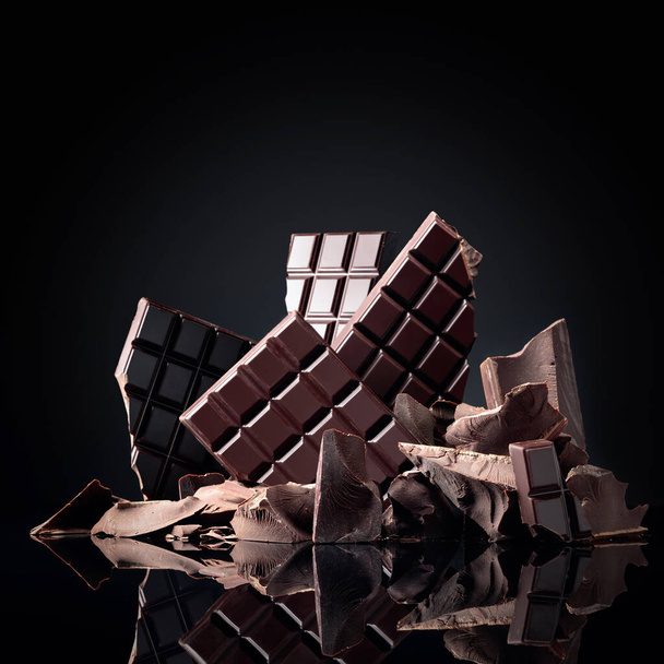 Chocolate bars and broken pieces of bitter black chocolate on a black background. - Photo, Image