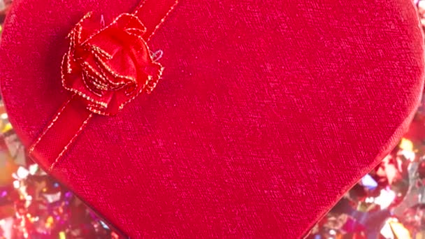Jelen vagy ajándék doboz szív alakú piros íj és konfetti vörös alapon - Felvétel, videó