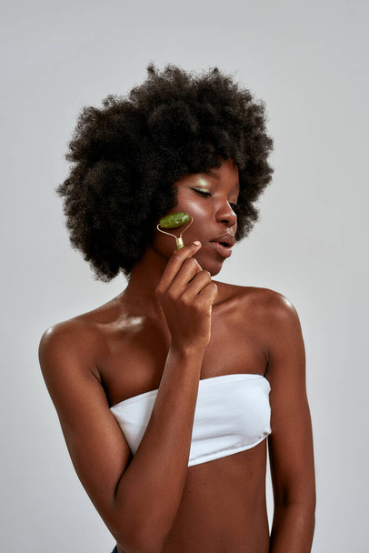 Attractive half naked young african american woman using jade roller or natural massage tool, posing isolated over gray background - Φωτογραφία, εικόνα