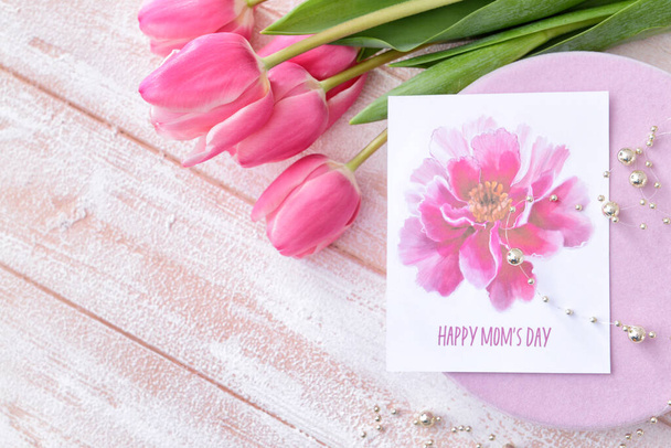 Hermosas flores, regalo y tarjeta de felicitación para el día de la madre sobre fondo de madera clara - Foto, Imagen