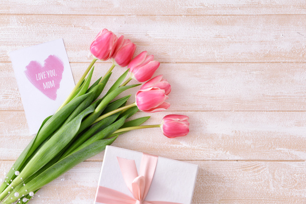 Hermosas flores, regalo y tarjeta de felicitación para el día de la madre sobre fondo de madera clara - Foto, imagen