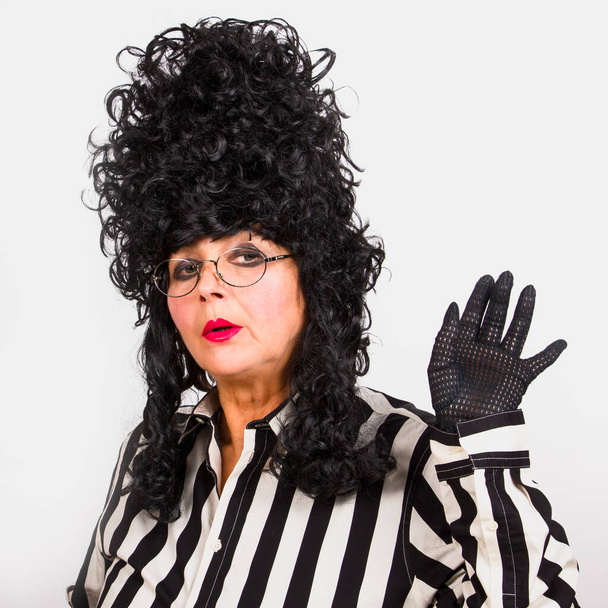Elegant woman in black baroque wig, black-white striped clothes and eyeglasses, waves his hand in a black fishnet glove. - Фото, изображение