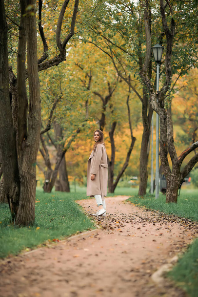 A European girl in a pink coat and blue jeans with holes walks in an autumn park - Foto, Bild