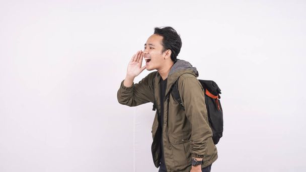 Joven estudiante con una bolsa gritando y gritando aislado en el fondo blanco - Foto, imagen