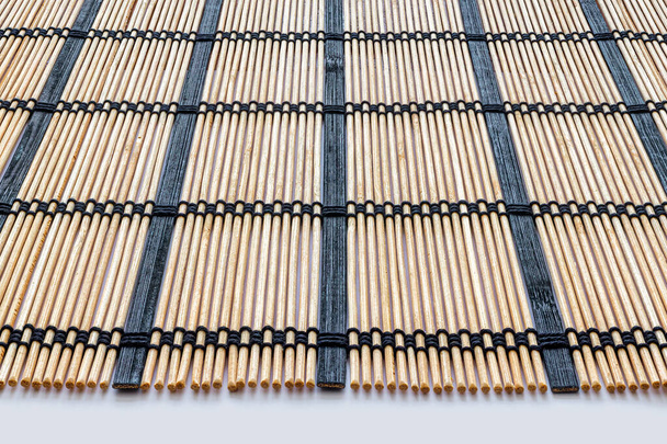 Στρώμα μπαμπού για την κατασκευή ρολού σούσι, από λεπτές ξύλινες ράβδους, που συγκρατείται μαζί με μαύρο νήμα - Φωτογραφία, εικόνα