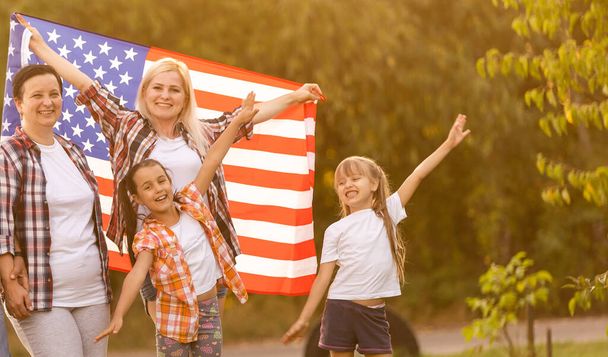 la grande famiglia cammina bandiere americane. Vista frontale, patrioti americani sul prato del parco. - Foto, immagini