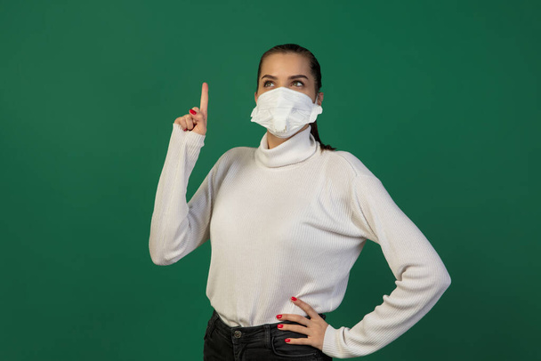 Woman in protective face mask isolated on green studio background. New rules of COVID spreading prevention - Zdjęcie, obraz