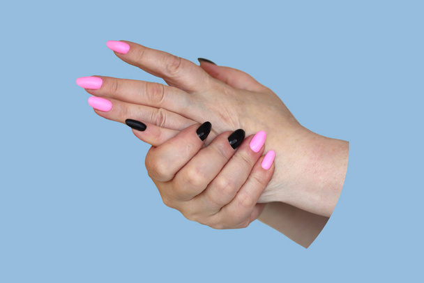 mani di una donna anziana con una manicure luminosa strofinare le unghie dipinte nero e rosa fuoco selettivo isolato, su uno sfondo grigio - Foto, immagini