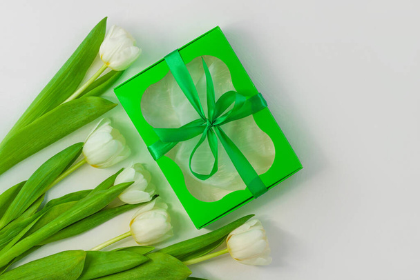 Bílé tulipánové květiny a zelená dárková krabice s mašlí na světlém pozadí ležely. Místo pro text 8. března Happy Womens Mothers Day.Flower kytice blahopřání. Kopírovat nápis horní části stránky. - Fotografie, Obrázek