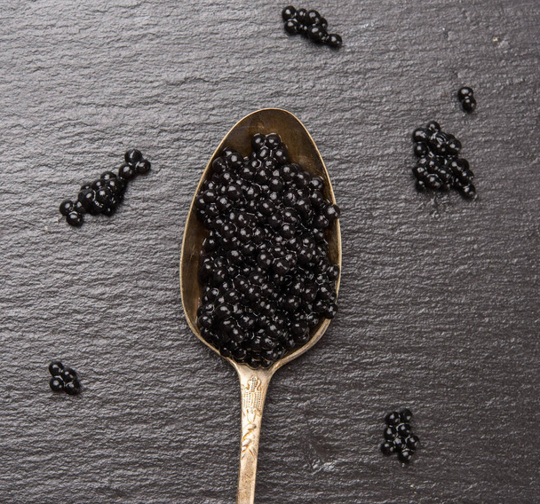 black caviar of paddlefish fish in a spoon, black background, top view - Foto, imagen