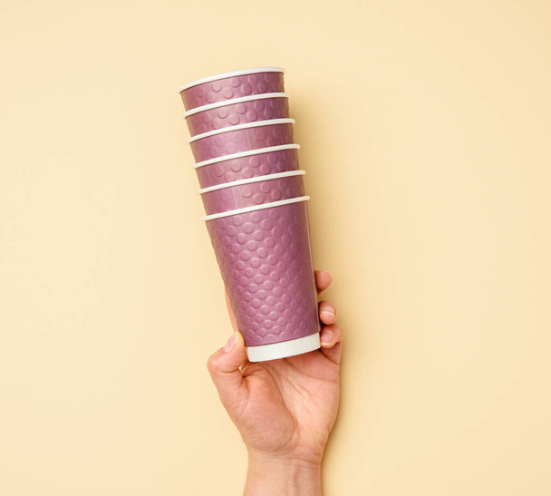 pila de mano femenina de vasos de papel desechables púrpura sobre fondo beige, cero residuos - Foto, imagen