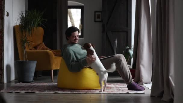 чоловік працює на аутсорсі з ноутбуком і грає з собакою одночасно вдома
 - Кадри, відео