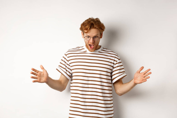 Impressed redhead man in glasses showing length of something big, demonstrate large size and looking amazed, standing over white background - Photo, Image