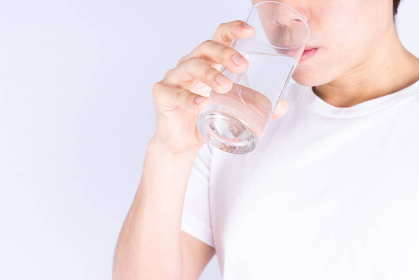 Άνθρωπος πόσιμο νερό απομονωμένο γκρι φόντο. Καθαρό πόσιμο νερό σε διαυγές γυαλί. - Φωτογραφία, εικόνα