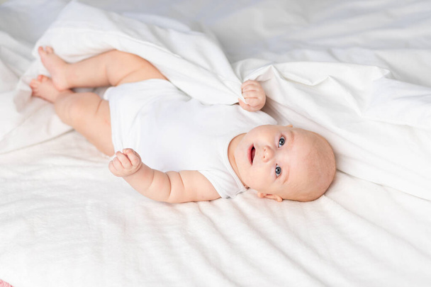 gelukkige baby op het bed in de ochtend. Textiel en beddengoed voor kinderen. Een pasgeboren baby is wakker geworden of gaat naar bed - Foto, afbeelding