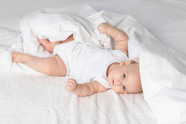 Baby auf dem Bett am Morgen. Textilien und Bettwäsche für Kinder. Ein Neugeborenes ist aufgewacht oder geht ins Bett - Foto, Bild