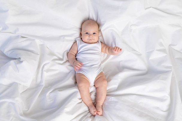 a child on a white bed in the morning. Textiles and bed linen for children. A newborn baby has woken up or is going to bed - Fotoğraf, Görsel