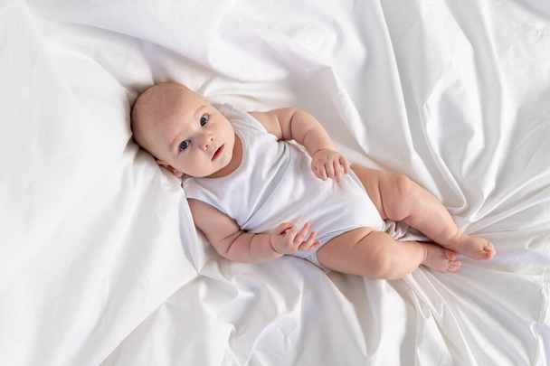 a child on a white bed in the morning. Textiles and bed linen for children. A newborn baby has woken up or is going to bed - Photo, image