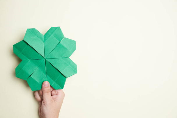 Trébol de cuatro hojas hecho de papel, origami, sostenido por una mano de una mujer joven sobre un fondo claro. Conceptos de suerte y el Día de San Patricio. Imagen con espacio de copia. - Foto, Imagen