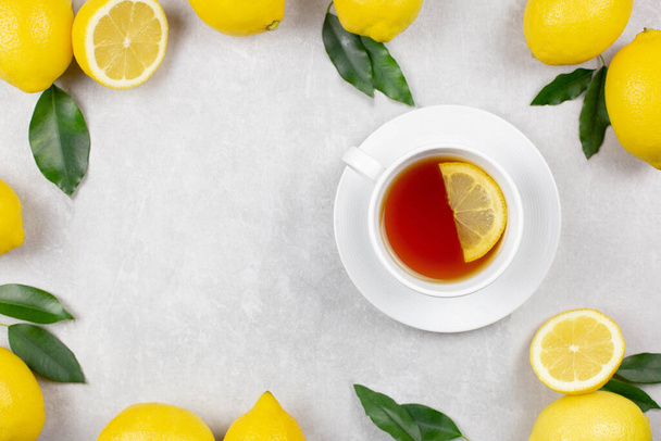 Чашка чая со свежими лимонами и листьями на белом бетонном фоне. Горячий здоровый напиток. Иммунная защита, витамин С. Копирование пространства. - Фото, изображение