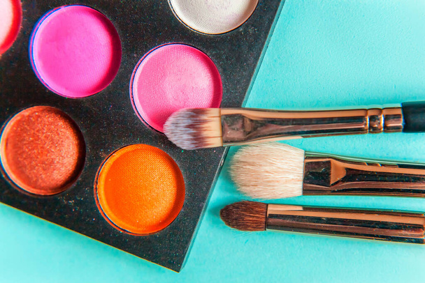 Tools for makeup and cosmetics different shades of eyeshadow palette and make up brush on trendy colorful blue pastel background. Top view flat lay and picturesque - Φωτογραφία, εικόνα