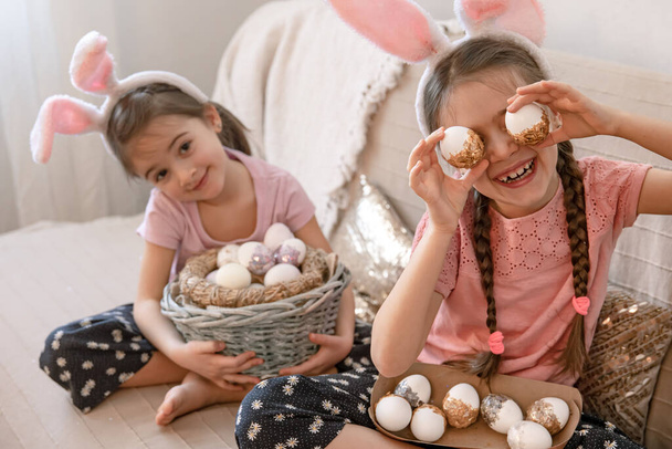 Nyuszifülű kishúgok, húsvéti tojásokkal a kanapén. A húsvéti ünnepre való felkészülés koncepciója. - Fotó, kép