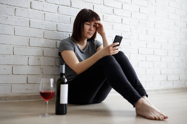 女性のアルコール依存症、関係、離婚、うつ病の概念-スマートフォンや飲酒ワインを使用して若い女性を強調 - 写真・画像