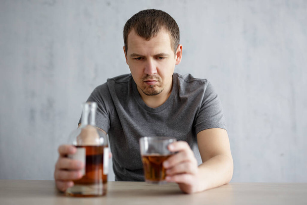 Alkoholismus und Depression - gestresster junger Mann sitzt mit Glas und Flasche Whiskey zu Hause oder in der Kneipe - Foto, Bild