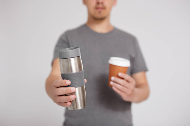 zero waste and eco friendly concept - thermo cup and disposable paper coffee cup in male hands over grey background with copy space - Photo, Image