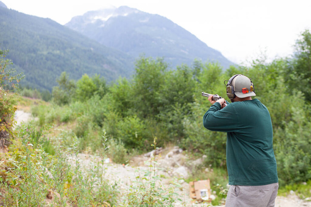 A man holds a shotgun downrange ready to fire at a clay pigeon to practice his aim in Squamish, British-Columbia - Zdjęcie, obraz