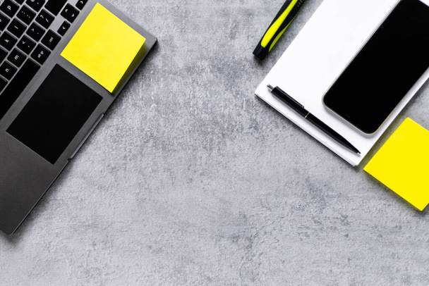 Laptop, phone, and office supplies on a gray concrete table. Workplace. A study table. Remote work. Distance learning. uminous yellow and extremely gray. The color of 2021. Copy space - Fotografie, Obrázek