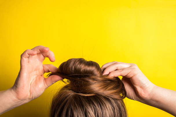 A woman makes a messy hair bun on her head. Yellow background. Copy space. Trend color of the year 2021 - Photo, Image